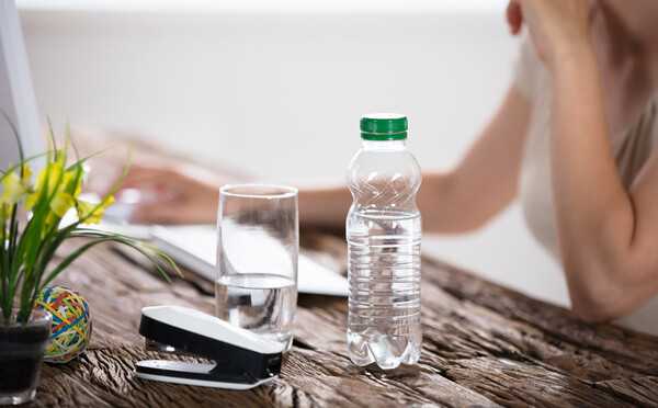 Vandens butelis šalia lengvo užkandžio ant šviesaus stalo